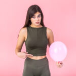 Beautiful young woman holding a pink balloon , feeling bloated concept , Woman having abdominal pain isolated on white