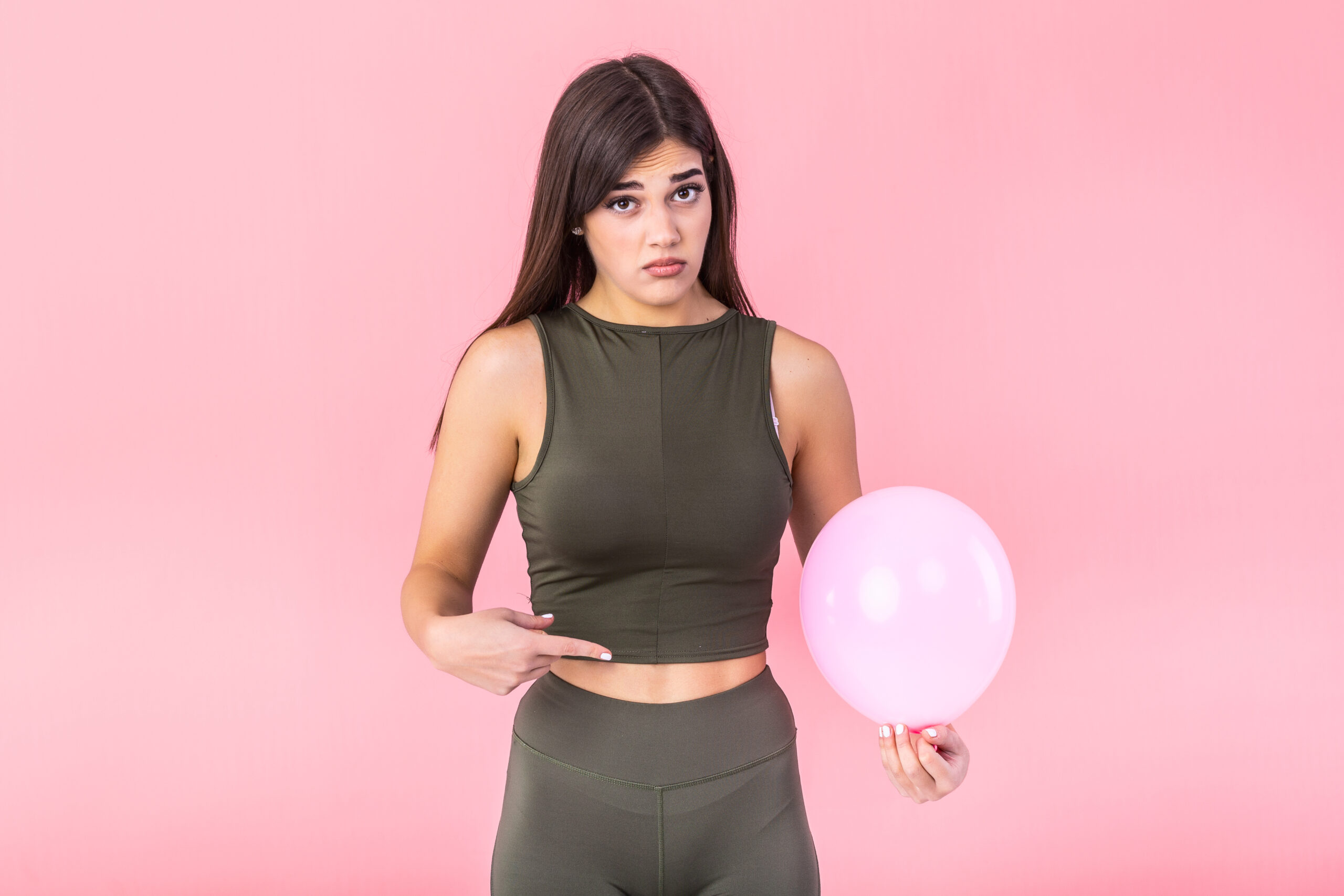 Beautiful young woman holding a pink balloon , feeling bloated concept , Woman having abdominal pain isolated on white
